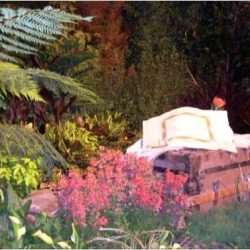 A stone bench surrounded by pink flowers and lush greenery in a garden setting.